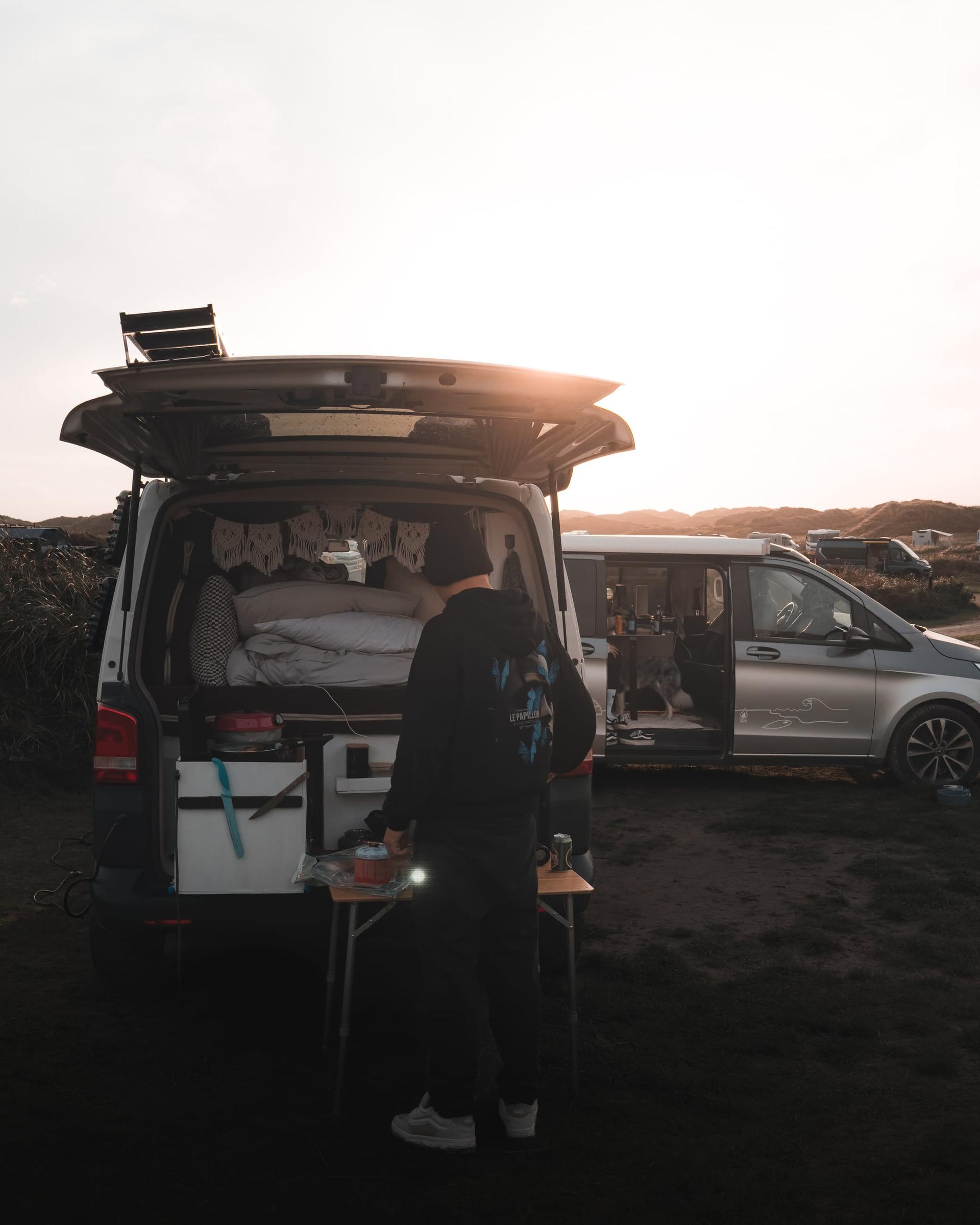 Eine Burg aus Campern wurde gebaut. Am Heck des vorderen Campers wird gegrillt bei Sonnenuntergang in den Dünen.